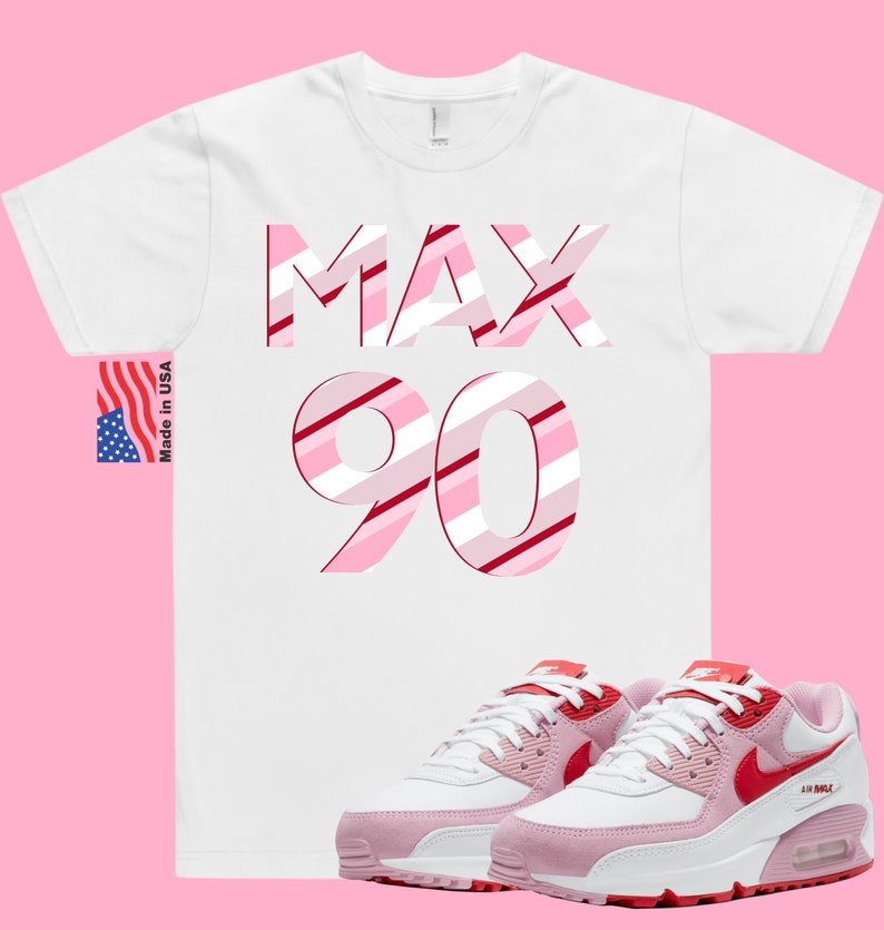 May include: White t-shirt with the words "MAX 90" in pink and red stripes.  Pink and white Nike Air Max 90 sneakers with red accents.