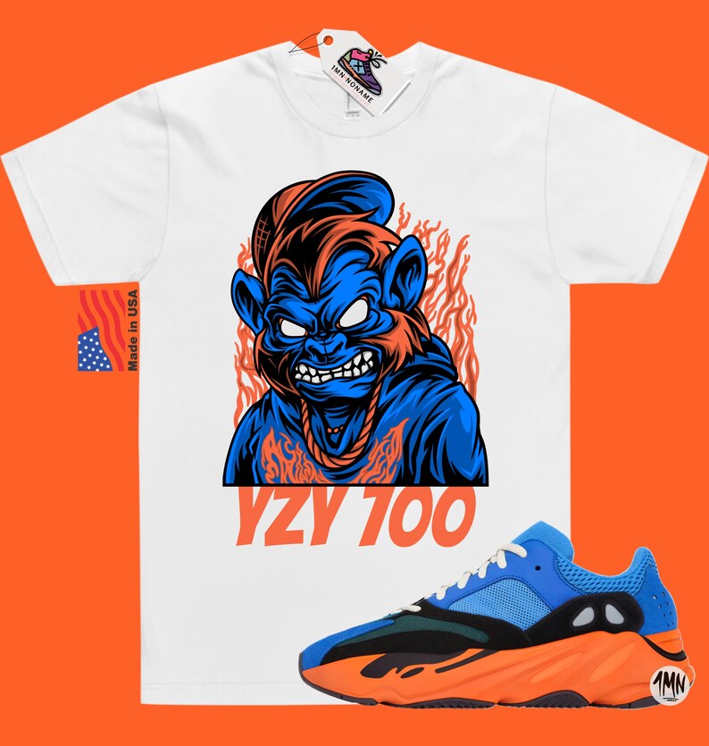 May include: White t-shirt with a blue and orange cartoon monkey graphic and the text "YZY 700". A pair of blue and orange Yeezy 700 sneakers are shown below the t-shirt.