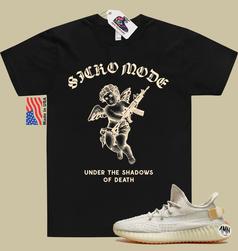 K&ouml;nnte beinhalten: Schwarzes T-Shirt mit einer wei&szlig;en Grafik eines Cherubins, der ein Gewehr h&auml;lt. Der Text "Sicko Mode" befindet sich &uuml;ber dem Cherubin und "Under the Shadows of Death" darunter. Ein Paar hellbeige Sneaker mit brauner Sohle befindet sich in der rechten unteren Ecke des Bildes.