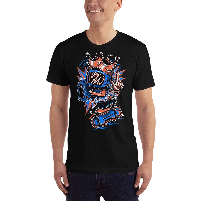 Pu&ograve; includere: Una maglietta nera con un'illustrazione di un personaggio dei cartoni animati che indossa un casco blu e una corona, mentre fa skateboard. Il personaggio indossa una camicia a motivi blu e arancioni e ha uno skateboard blu e arancione.