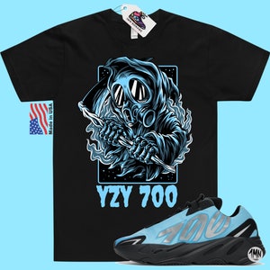 May include: Black t-shirt with a graphic of a blue hooded figure wearing a gas mask and holding a scythe. The text "YZY 700" is printed below the graphic. A pair of blue and black Yeezy 700 sneakers are also pictured.