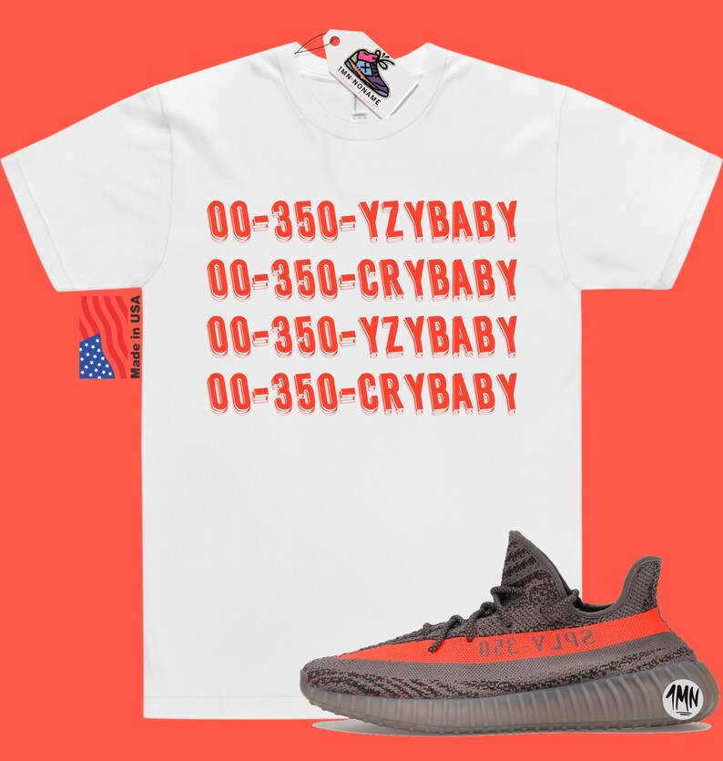 Peut inclure: T-shirt blanc avec du texte rouge qui dit "00-350-YZYBABY" et "00-350-CRYBABY" r&eacute;p&eacute;t&eacute; deux fois. Une paire de baskets grises et orange est repr&eacute;sent&eacute;e sous le t-shirt.