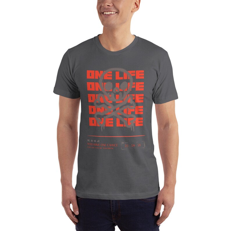 Puede incluir: Una camiseta gris oscuro con un gr&aacute;fico de calavera y huesos cruzados rojos y el texto "ONE LIFE" repetido cuatro veces. El texto est&aacute; en una fuente de estilo graffiti. La parte inferior de la camiseta tiene el texto "YOU HAVE ONE CHANCE" en una fuente m&aacute;s peque&ntilde;a.