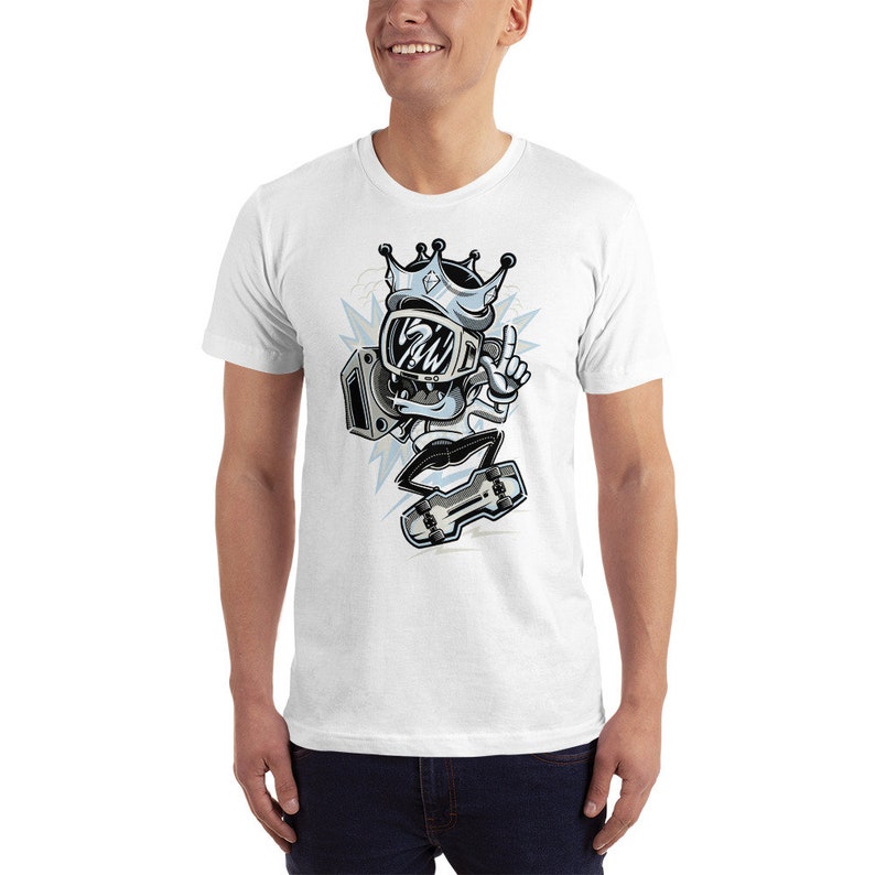 Puede incluir: Camiseta blanca con una ilustraci&oacute;n de dibujos animados de un personaje que lleva una corona y un casco, sosteniendo una patineta y apuntando con un dedo. El personaje est&aacute; en una pose de patinaje.