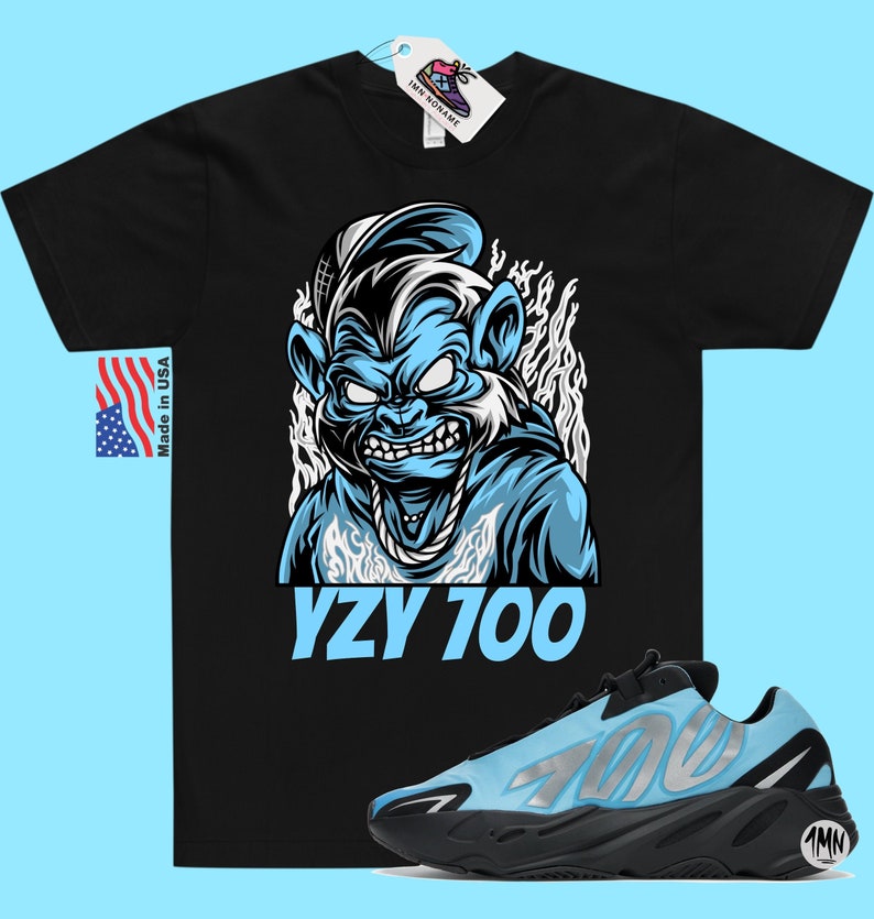 May include: Black t-shirt with a blue cartoon monkey wearing a sailor hat and a gold chain. The text "YZY 700" is printed below the monkey. A pair of blue and black Yeezy 700 sneakers are shown below the t-shirt.