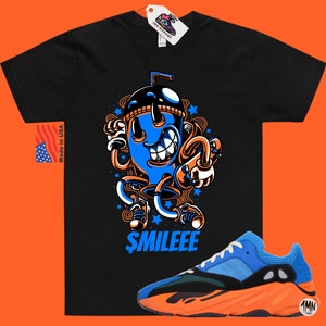 May include: Black t-shirt featuring a cartoon illustration of a blue and orange drink with a straw and the text "$MILEEE". A pair of blue and orange trainers with a black sole.