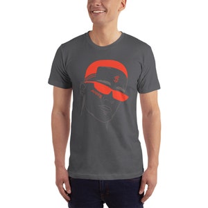 May include: A dark gray t-shirt with a red illustration of a person wearing a red hat with a dollar sign and red sunglasses. The text "SOMED" is written on the sunglasses.