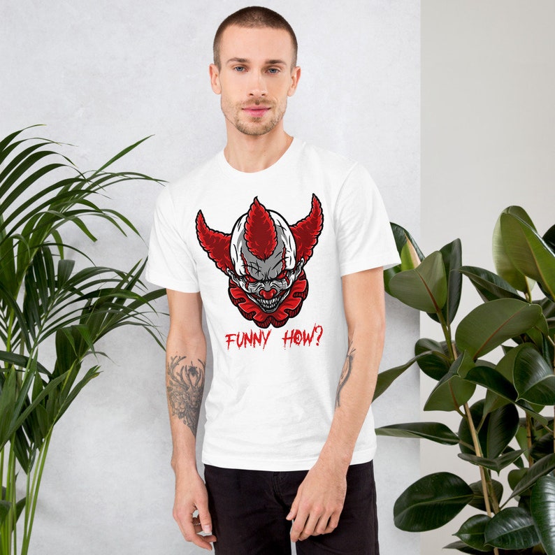 May include: White t-shirt with a graphic of a scary clown with red hair and the text "FUNNY HOW?" printed on the front.