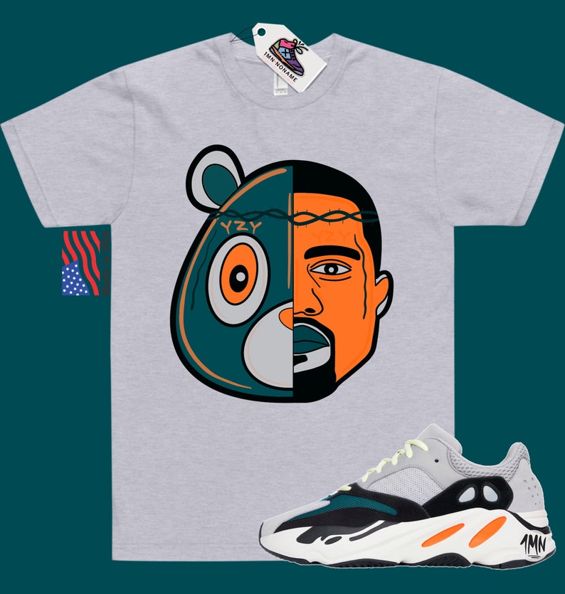 May include: A grey t-shirt with a graphic of a cartoon bear and Kanye West's face. The graphic is split down the middle, with the bear on the left and Kanye on the right. The bear is wearing a crown of thorns. The t-shirt is paired with a pair of white, black, and orange sneakers with the text "YZY" on the side.