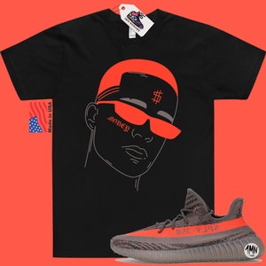 May include: Black t-shirt with a red outline of a person wearing sunglasses and a hat with a dollar sign on it. The text "Money" is on the person's cheek. A pair of grey and orange Yeezy sneakers are in the bottom right corner of the image.