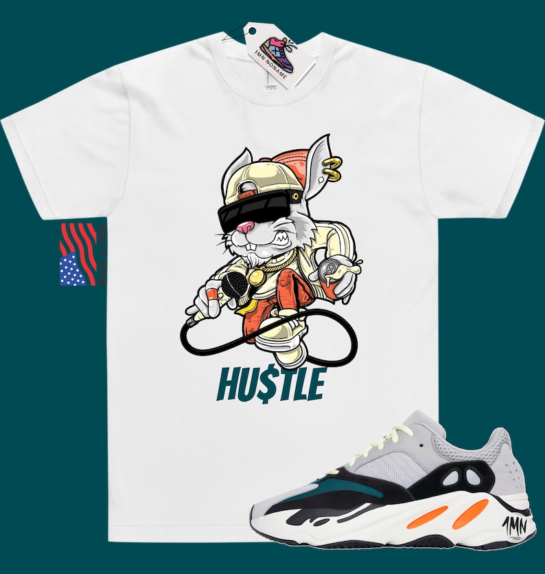 May include: White t-shirt featuring a cartoon rabbit wearing a backwards cap, sunglasses, and a gold chain. The rabbit is holding a microphone and a spray can. The text "HUSTLE" is printed below the rabbit. A pair of grey, green, and orange trainers are shown below the t-shirt.