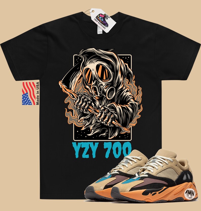 May include: Black t-shirt with a graphic of a hooded figure wearing a gas mask and holding a scythe. The text "YZY 700" is printed below the graphic. A pair of tan and orange sneakers with blue accents are shown in the bottom right corner of the image.