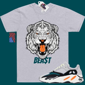 May include: A grey t-shirt with a white lion graphic and the word "BEAST" printed on the front. A pair of light grey, black, and orange trainers with the word "Yeezy" on the side.