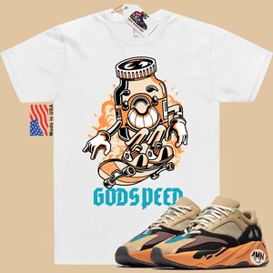 May include: White t-shirt with a cartoon illustration of a pill bottle skateboarding with the text "Godspeed". A pair of tan, black, and orange sneakers with a blue accent are shown below the t-shirt.