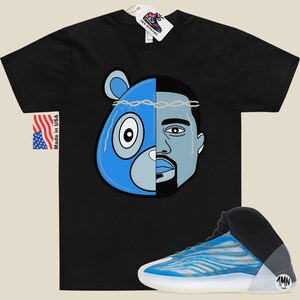 May include: Black t-shirt with a blue and grey illustration of a bear head and a man's face. The text "1MN" is on the side of a blue and white sneaker.