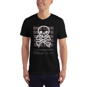 May include: Black t-shirt with a white skull and crossbones graphic. The graphic is stylized to look like spray paint. The text "ONE LIFE" is repeated multiple times in a faded gray color. The text "YOU HAVE ONE CHANCE" and "23:59:59" are also printed on the shirt.