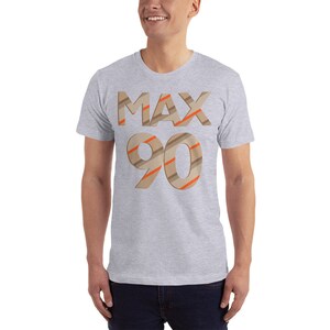 May include: A grey t-shirt with the text "MAX 90" printed on the front. The text is in a brown and orange striped font.