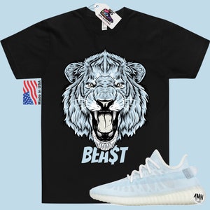 Peut inclure: T-shirt noir avec un motif de lion blanc et le mot "BEAST" imprim&eacute; en dessous. Le lion a une expression f&eacute;roce, la gueule ouverte et les dents apparentes. Une paire de baskets bleu clair et blanches est repr&eacute;sent&eacute;e sous le t-shirt.