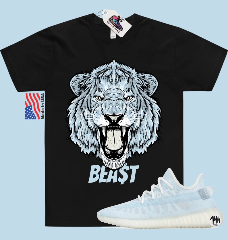 Peut inclure: T-shirt noir avec un motif de lion blanc et le mot "BEAST" imprim&eacute; en dessous. Le lion a une expression f&eacute;roce, la gueule ouverte et les dents apparentes. Une paire de baskets bleu clair et blanches est repr&eacute;sent&eacute;e sous le t-shirt.