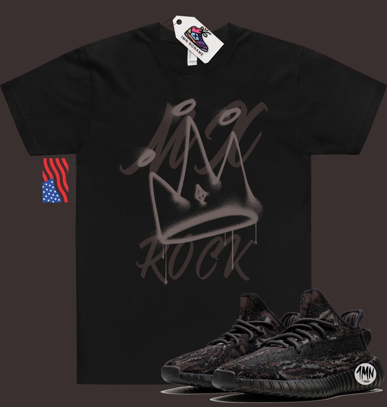 Puede incluir: Camiseta negra con una corona pintada con aerosol y la palabra "ROCK" en blanco. Un par de zapatillas negras y marrones con estampado de camuflaje se muestran debajo de la camiseta.