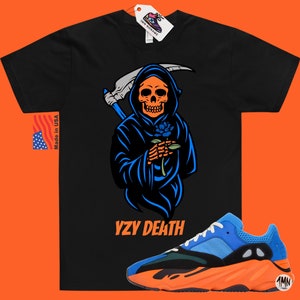 May include: Black t-shirt featuring a Grim Reaper design with a blue rose, the text "YZY DEATH" is below the graphic. A pair of blue and orange trainers are at the bottom. The tag says "1MN RONAME" and "Made in USA".