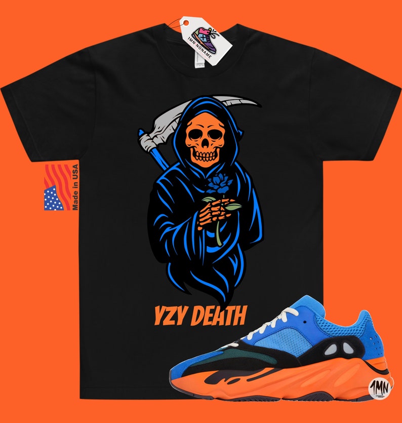 May include: Black t-shirt featuring a Grim Reaper design with a blue rose, the text "YZY DEATH" is below the graphic. A pair of blue and orange trainers are at the bottom. The tag says "1MN RONAME" and "Made in USA".