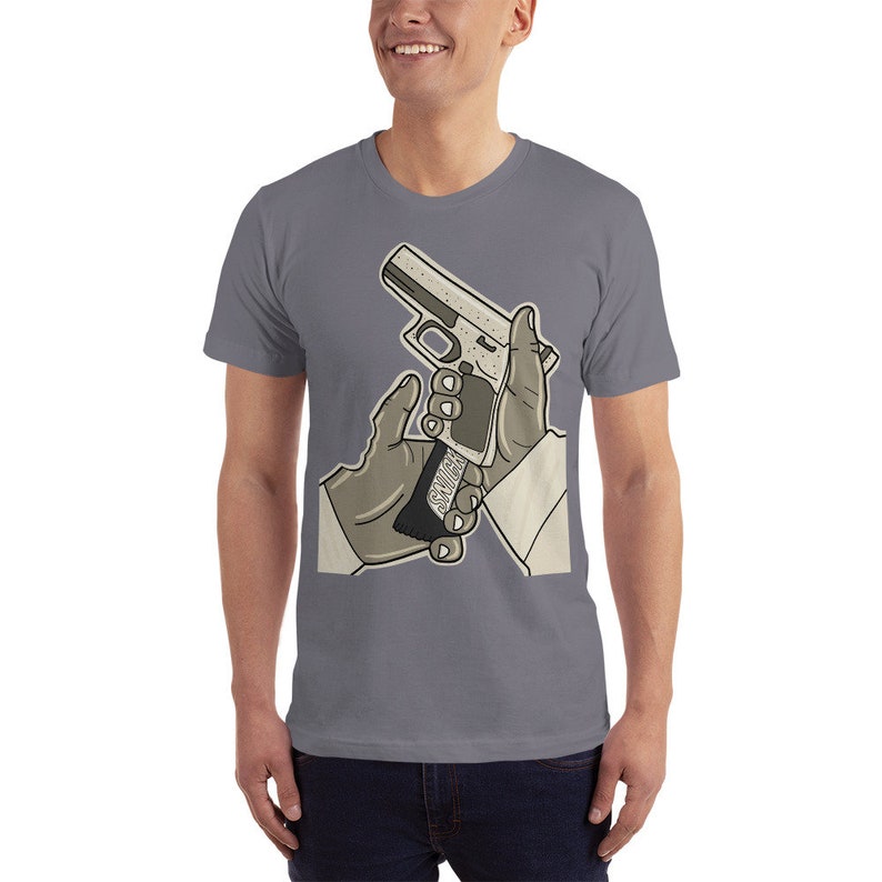 K&ouml;nnte beinhalten: Ein graues T-Shirt mit einem Aufdruck von zwei sich sch&uuml;ttelnden H&auml;nden, wobei eine Hand eine silberne Pistole mit dem Wort "SAVAGE" auf der Seite h&auml;lt.