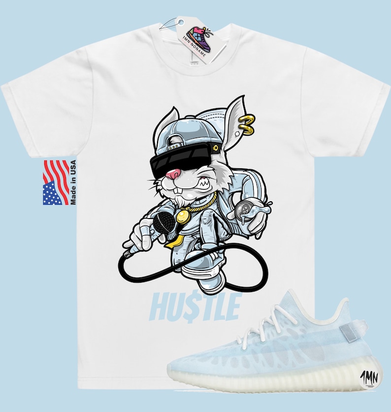 May include: White t-shirt featuring a cartoon rabbit wearing sunglasses and a backwards hat holding a microphone. The text "HUSTLE" is printed below the rabbit. A pair of light blue and white trainers are shown below the t-shirt.