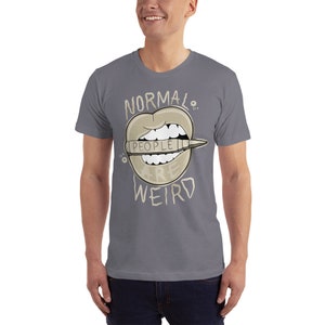 Pode incluir: Uma camiseta cinza com um gr&aacute;fico de uma boca com um l&aacute;pis que diz "As pessoas s&atilde;o estranhas". O texto "Normal." est&aacute; acima da boca e o texto "WEIRD" est&aacute; abaixo da boca.