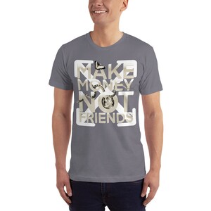 K&ouml;nnte beinhalten: Ein graues T-Shirt mit einem wei&szlig;en Grafikdesign, auf dem "MAKE MONEY NOT FRIENDS" steht. Das Grafikdesign zeigt einen Schmetterling, eine Schlange und ein menschliches Gesicht.