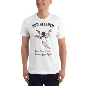 May include: White t-shirt with a black and white illustration of a cherub wearing a ski mask and holding a gun and a lit Molotov cocktail. The text "GOD BLESSED" is above the cherub and the text "Now And forever Under Your Spell" is below the cherub.