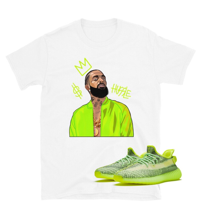 Puede incluir: Una camiseta blanca con una ilustraci&oacute;n de dibujos animados de un hombre que lleva una chaqueta verde ne&oacute;n y una cadena de oro. El texto "HUSTLE" est&aacute; escrito en verde ne&oacute;n sobre la cabeza del hombre. Una corona y un signo de d&oacute;lar est&aacute;n por encima del texto. Un par de zapatillas de deporte verde ne&oacute;n y negras est&aacute;n debajo de la camiseta.