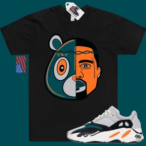 May include: Black t-shirt with a graphic of Kanye West's face and the Yeezy bear logo. The graphic is split in half, with Kanye's face on the right and the bear on the left. The bear is teal and orange, and Kanye's face is orange. The t-shirt is paired with a pair of white, orange, and teal sneakers with the text "YZY" on the side.