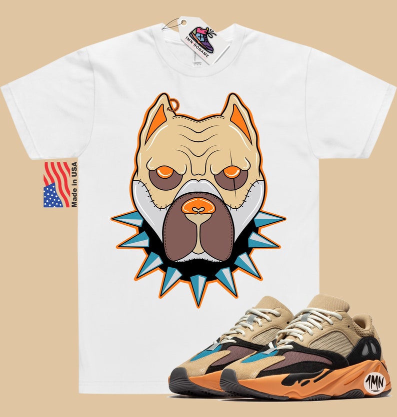 May include: White t-shirt with a cartoon illustration of a dog's face wearing a spiked collar. The dog has brown eyes, a brown nose, and a brown mouth. The t-shirt is paired with a pair of tan, black, and blue sneakers with the text "1MN" on the side.