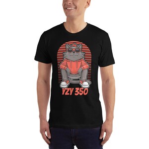 Pode incluir: Camiseta preta com uma ilustra&ccedil;&atilde;o de desenho animado de um gato cinza usando &oacute;culos de sol vermelhos, um moletom vermelho e t&ecirc;nis brancos. O gato est&aacute; sentado com as pernas cruzadas. O fundo &eacute; um p&ocirc;r do sol vermelho e branco com o texto "YZY 350" em vermelho.