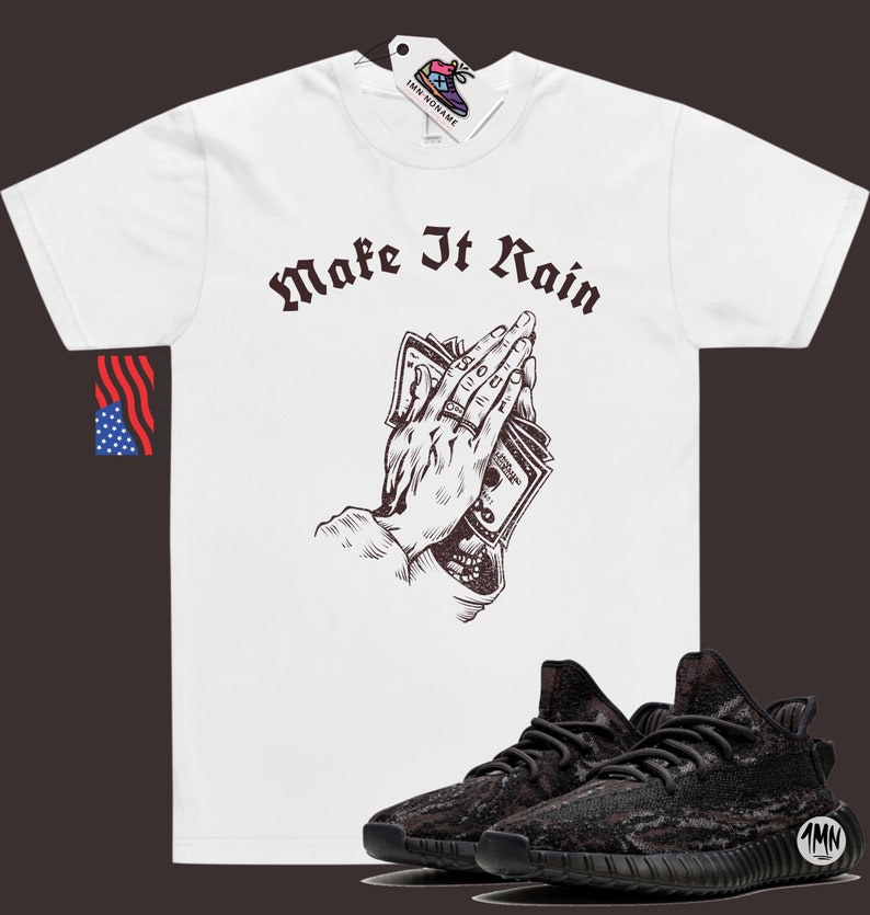 K&ouml;nnte beinhalten: Wei&szlig;es T-Shirt mit einer braunen Grafik einer Hand, die Geld h&auml;lt, mit dem Text "Make It Rain" in Braun. Schwarze und graue Sneaker mit einem Tarnmuster.