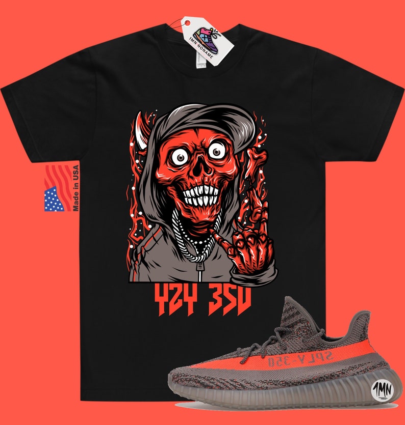 Może przedstawiać: Czarny T-shirt z czerwoną i szarą ilustracją czaszki w kapturze i łańcuchu. Tekst "424 350" jest nadrukowany pod ilustracją. Para szarych i pomarańczowych but&oacute;w Yeezy Boost 350 V2 jest pokazana pod T-shirtem.