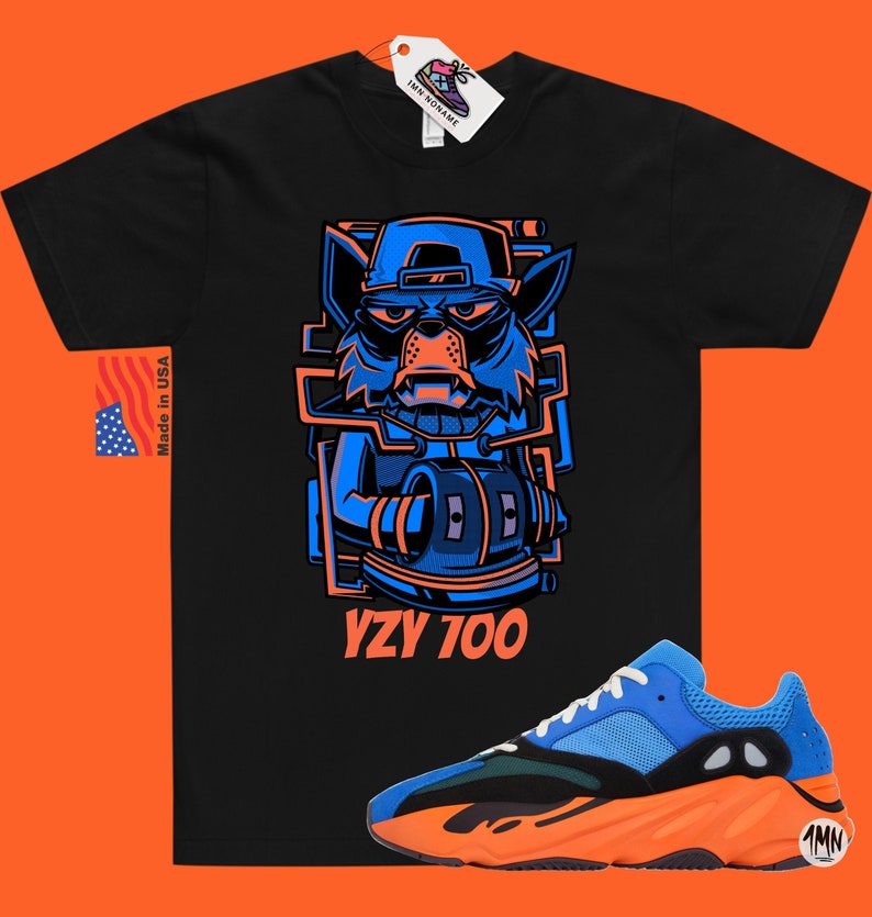 Puede incluir: Camiseta negra con un lobo de dibujos animados azul y naranja y el texto "YZY 700". Un par de zapatillas azules y naranjas con suela negra.