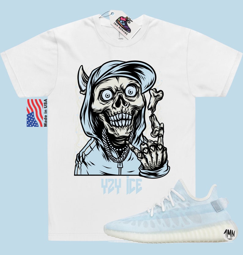 May include: White t-shirt with a graphic of a cartoon skeleton wearing a blue hoodie and a baseball cap. The skeleton is holding a bone in its hand and has the words "YZY ICE" printed below it. A pair of light blue and white sneakers are also pictured.