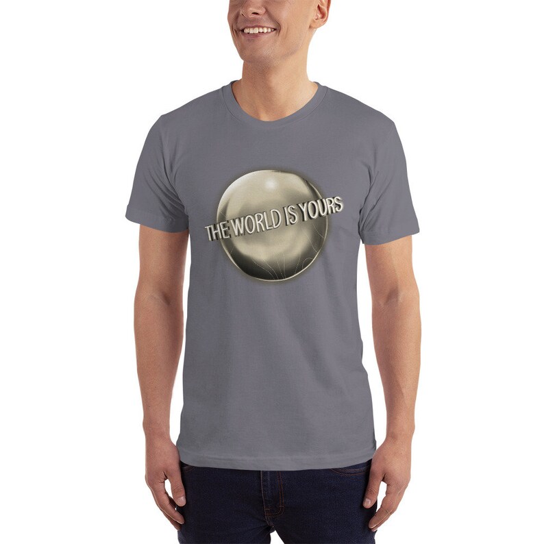 May include: A gray t-shirt with a silver globe graphic and the text "THE WORLD IS YOURS" printed on the front.