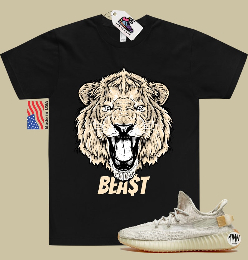 May include: Black t-shirt with a graphic of a lion's head and the word "BEAST" printed in beige. A pair of beige Yeezy sneakers with a tan sole are shown below the t-shirt.