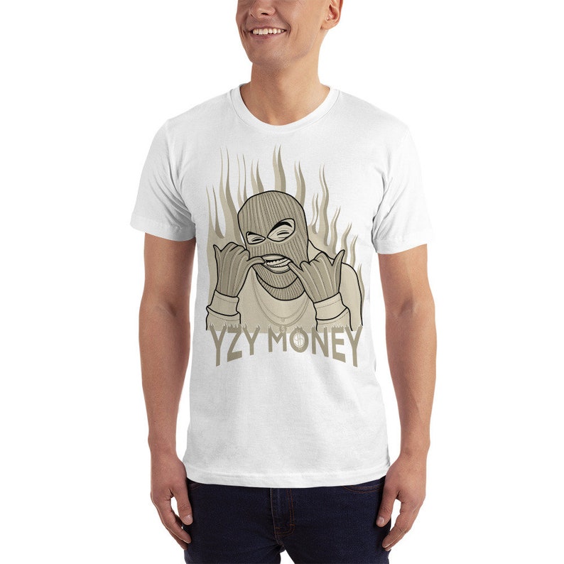 May include: White t-shirt with a graphic of a person wearing a ski mask and a gold chain, with flames behind them. The text "YZY MONEY" is printed below the graphic.
