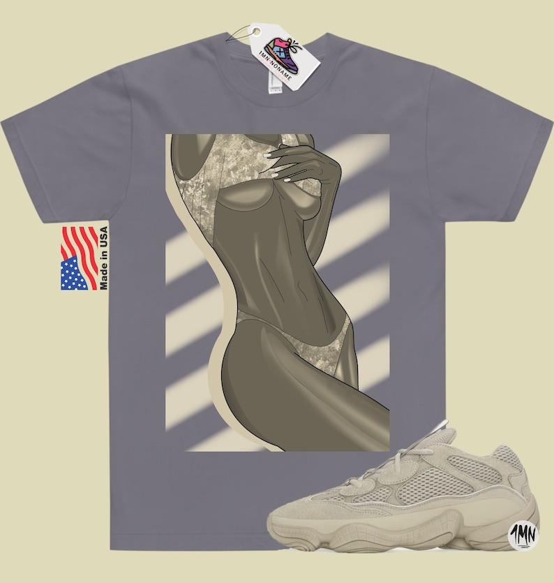 Puede incluir: Una camiseta gris con un gr&aacute;fico de una mujer en traje de ba&ntilde;o. La camiseta tiene una etiqueta que dice "1MN" y las palabras "Made in USA". Tambi&eacute;n se muestra un par de zapatillas beige con una parte superior de malla y una suela gruesa.