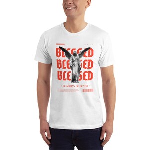 May include: White t-shirt with a red graphic print of an angel with wings and the word "Blessed" repeated four times. The text "Guardian of Death" is printed below the angel.