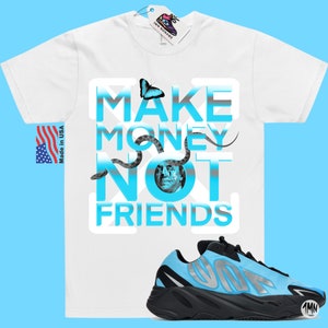 May include: White t-shirt with a blue and grey graphic that says "Make Money Not Friends". A blue and black sneaker with a silver accent is in the bottom right corner of the image.