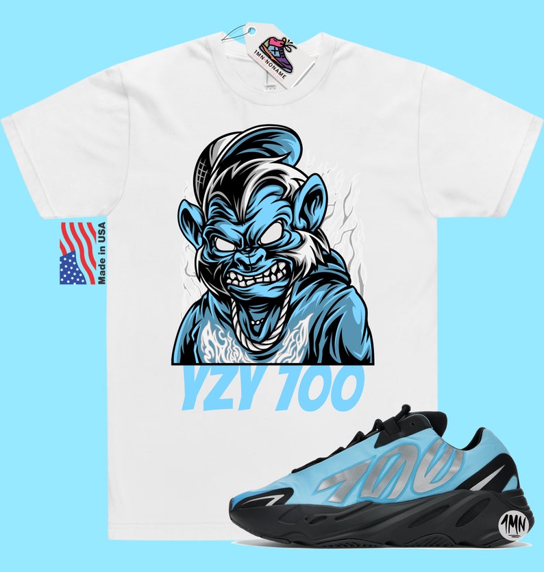 May include: A white t-shirt with a blue cartoon monkey wearing a hat and a chain. The text "YZY 700" is printed below the monkey. A pair of blue and black Yeezy 700 sneakers are shown below the t-shirt.