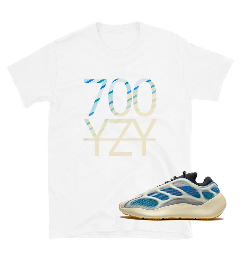 Puede incluir: Camiseta blanca con "700 YZY" impreso en rayas azules y verdes. Un par de zapatillas blancas y azules con suela amarilla.