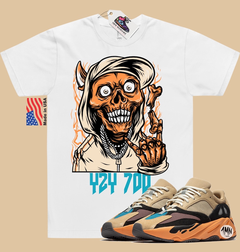 May include: White t-shirt with a cartoon illustration of a skull wearing a hoodie and holding a bone. The text "424 700" is printed below the illustration. A pair of tan, orange, and black sneakers with blue accents are shown below the t-shirt.