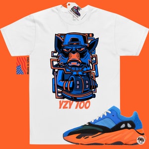 Puede incluir: Camiseta blanca con un gr&aacute;fico de lobo de dibujos animados azul y naranja y el texto "YZY 700". Un par de zapatillas azules, naranjas y verdes con el texto "1MN" en el lateral.