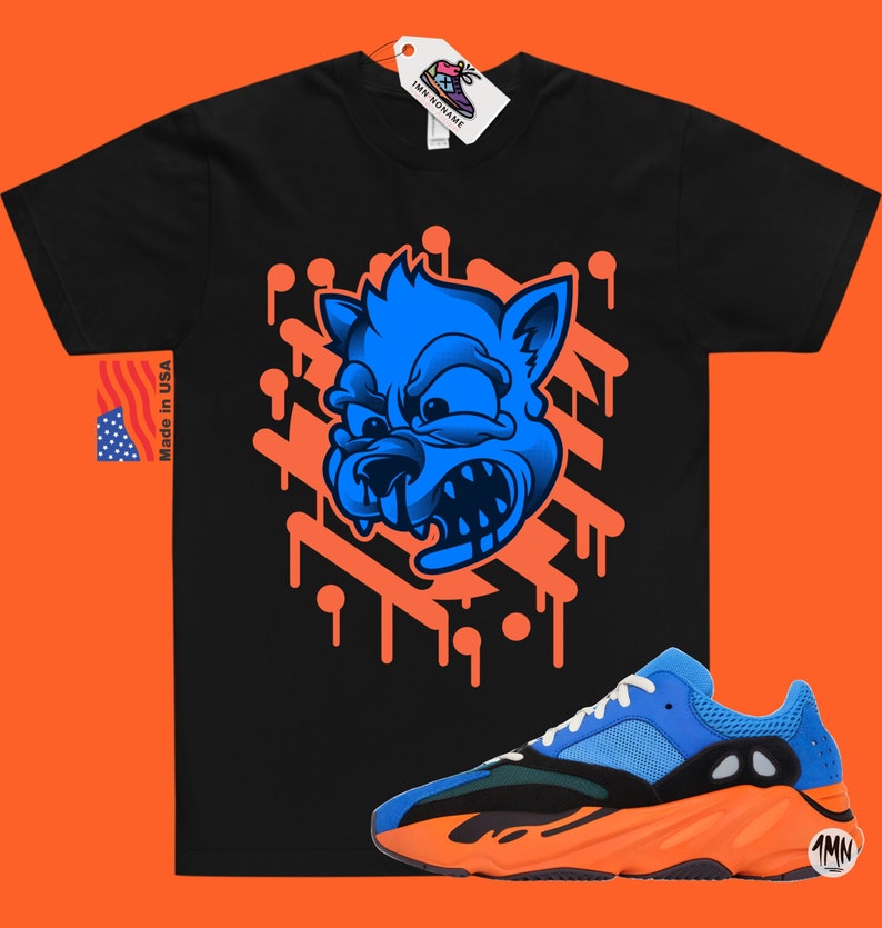 May include: A black t-shirt with a blue cartoon wolf graphic and orange dripping paint. The shirt is paired with blue and orange sneakers with the text "1MN" on the side.